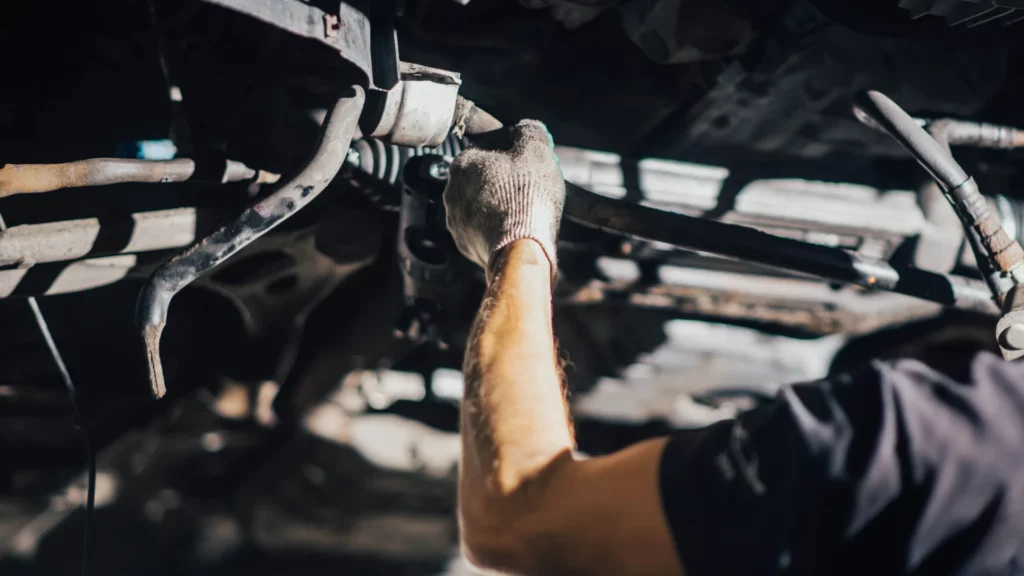 Zdjęcie przedstawia technika wykonującego naprawę układu kierowniczego, w tym wymianę uszkodzonych elementów.