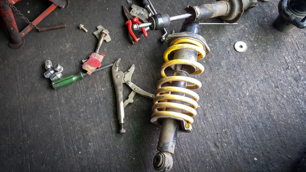 Zdjęcie przedstawia leżące na ziemi zdemontowane amortyzatory i narzędzia