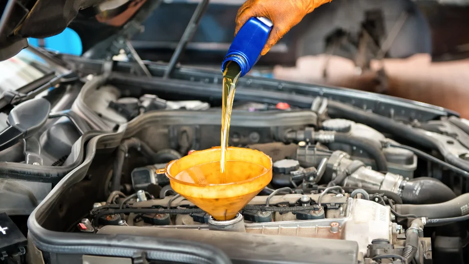 Zdjęcie przedstawia proces dolewania oleju do silnika za pomocą żółtego lejka.