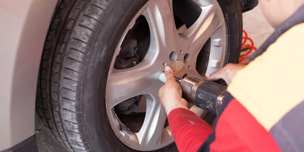 Zdjęcie przedstawia proces odkręcania koła samochodowego w celu naprawy opony.