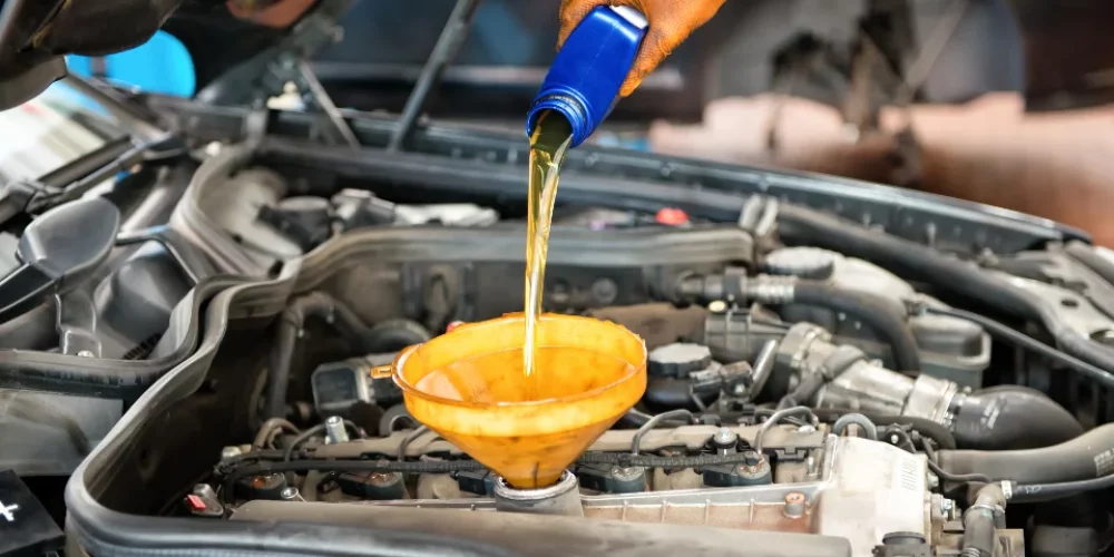 Zdjęcie przedstawia proces dolewania oleju do silnika za pomocą żółtego lejka.